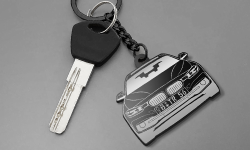 Car key with stylized front view keychain: black grille, headlights, and bat symbol on hood