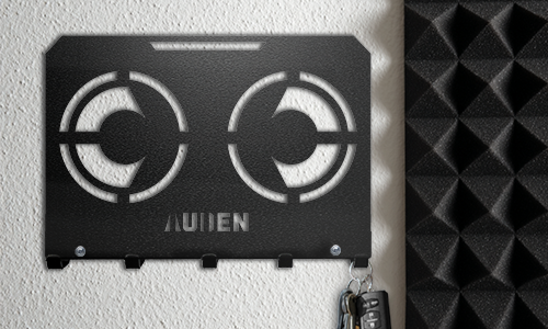 Portallaves de pared de metal con diseño geométrico recortado y nombre personalizado, montado en una pared texturizada