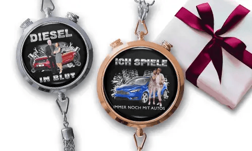 Zwei Taschenuhren mit Auto-Designs und deutschem Text. Eine sagt „Diesel im Blut“ mit einem roten Auto. Die andere hat „Ich spiele immer noch mit Autos“ und ein blaues Auto. Sie befinden sich neben einem verpackten Geschenk mit rotem Band und vermitteln ein verspieltes Automobilthema.