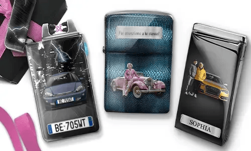 Drei Metallfeuerzeuge mit personalisierten Designs. Das linke Feuerzeug zeigt eine Stadtsilhouette und ein Paar neben einem Auto mit der Aufschrift „BESTE OMA DER WELT“. Das mittlere Feuerzeug stellt ein rosafarbenes Oldtimer-Auto dar, darüber steht „HAB DICH LIEB OMA“. Das rechte Feuerzeug zeigt ein blaues Auto und ein Kennzeichen. Rosafarbene Schleifen verleihen dem Ganzen einen Geschenkcharakter.