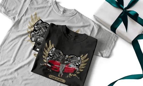 Zwei T-Shirts mit rotem Sportwagen, goldenen Flügeln, Schädeln und BORN TO DRIVE Banner, neben Geschenkbox