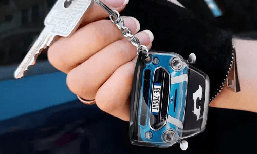Käsi pitää avaimenperää, joka on muotoiltu siniseksi autoksi yksityiskohtaisella etuosalla