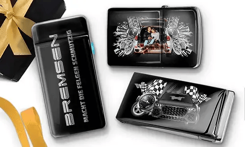Elegante schwarze Feuerzeuge mit Auto-Designs. Eines zeigt eine Familie in einem Auto, ein anderes ein blaues Auto mit karierten Flaggen. Daneben liegt eine Geschenkbox mit goldener Schleife.