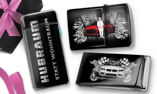Drei Zigarettenetuis in Schwarz und Silber mit dynamischen Auto-Grafiken. Eines trägt die Aufschrift „Hubraum statt Wohntraum“, während die anderen Rennmotive zeigen.