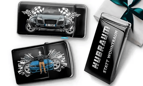 Geschenkset mit Auto-Themen-Metallbehältern, die Bilder eines grünen Sportwagens, karierten Flaggen und Motor-Motiven zeigen. Enthält ein Zigarettenetui mit der Aufschrift „Hubraum Statt Wohntraum“.