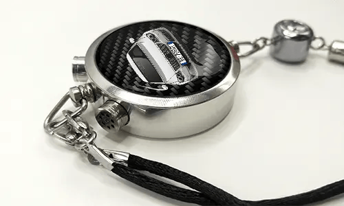 Round car key fob with carbon fiber face, buttons labeled LOCK and UNLOCK, braided black cord attached